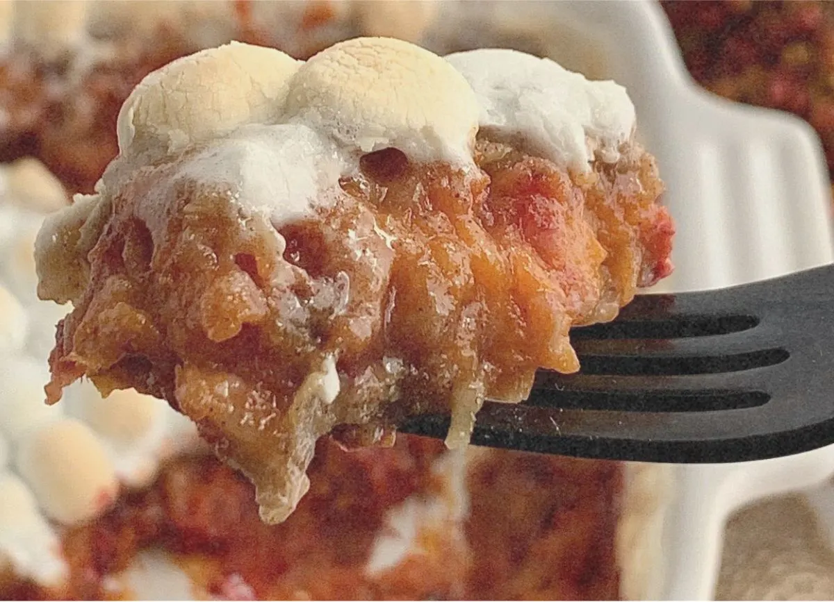 A fork holding a bite of yummy sweet potato casserole.