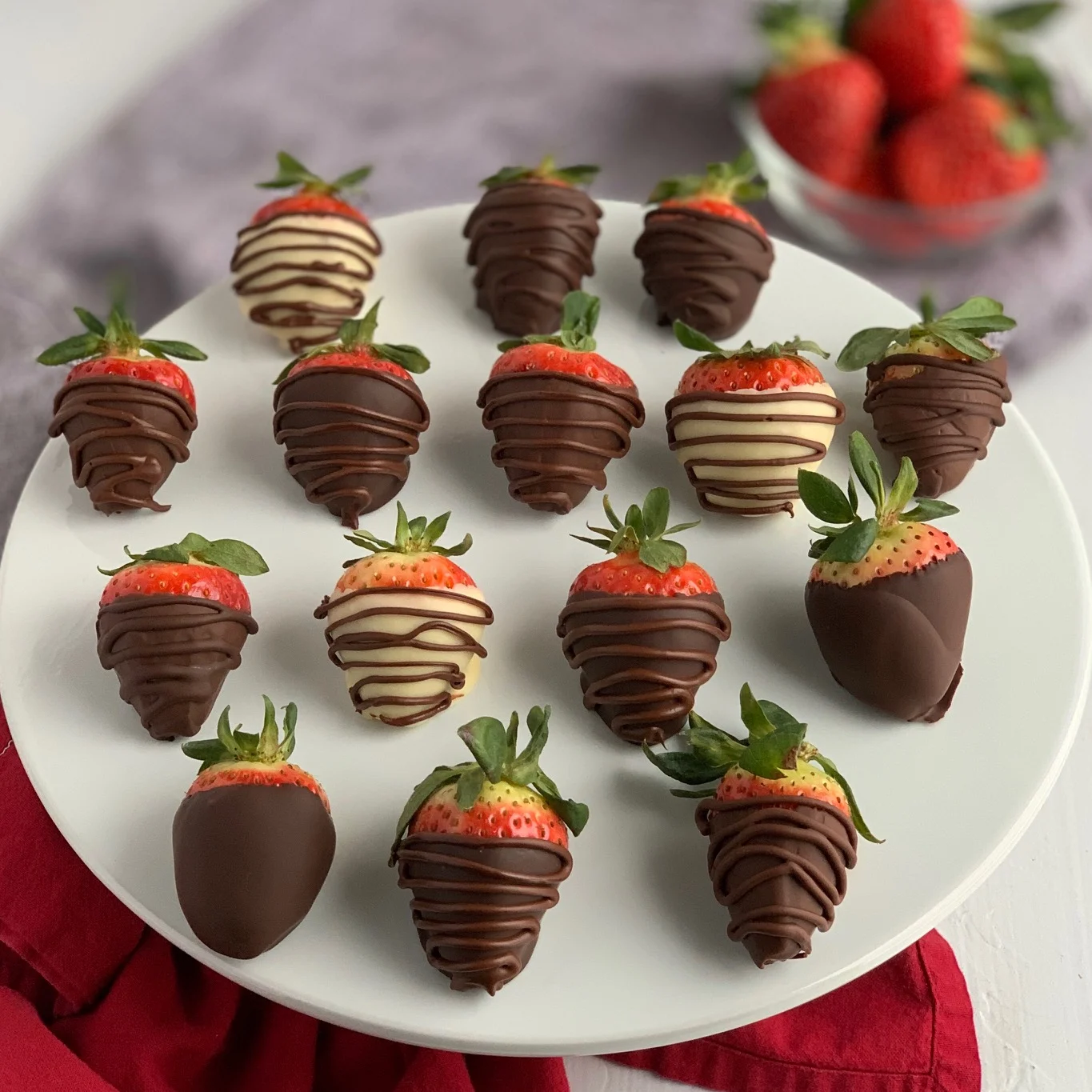 A cake plate with chocolate covered strawberries on it.