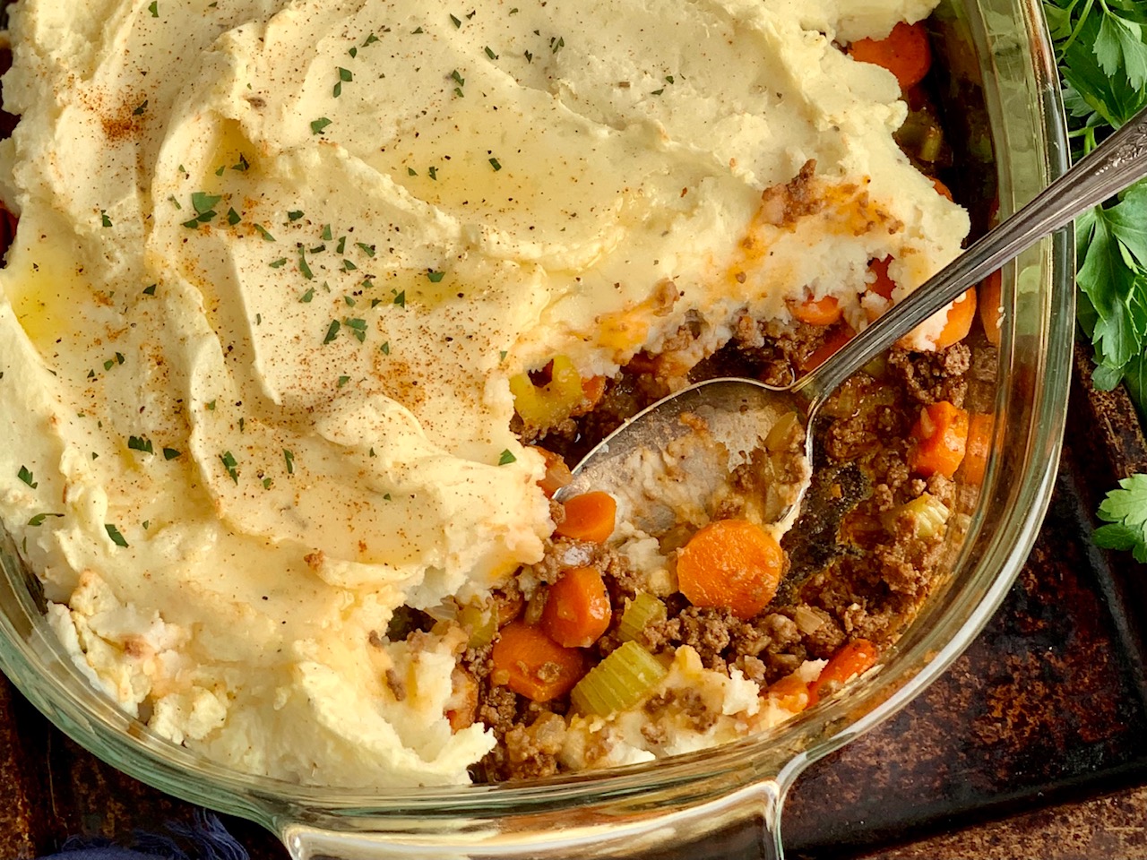 A glass 9x13-inch pan with a celery, carrot, and ground beef mixture topped with creamy and thick mashed potatoes. A spoon has scooped some of the pie out and is in the dish.