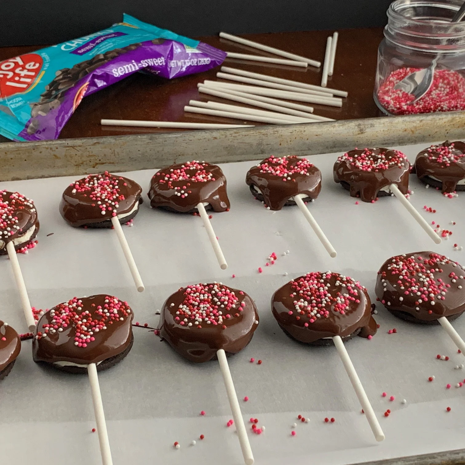 Chocolate dipped gluten and dairy free ores on a stick with festive white, pink, and red sprinkles. 