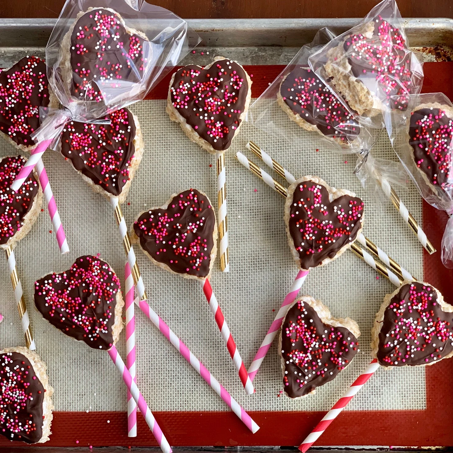 Rice krispies cut into the shape of a heart with melted chocolate and sprinkles on them.