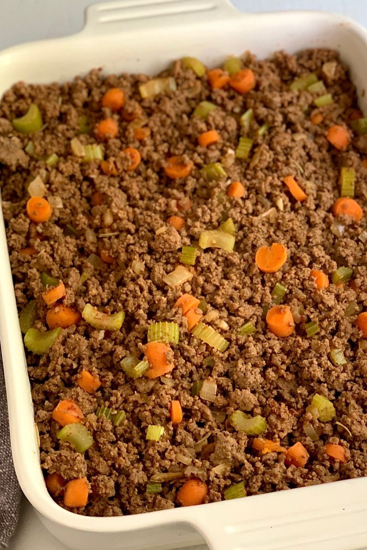 A baking dish with cooked beef, onions, carrots, celery in it. 