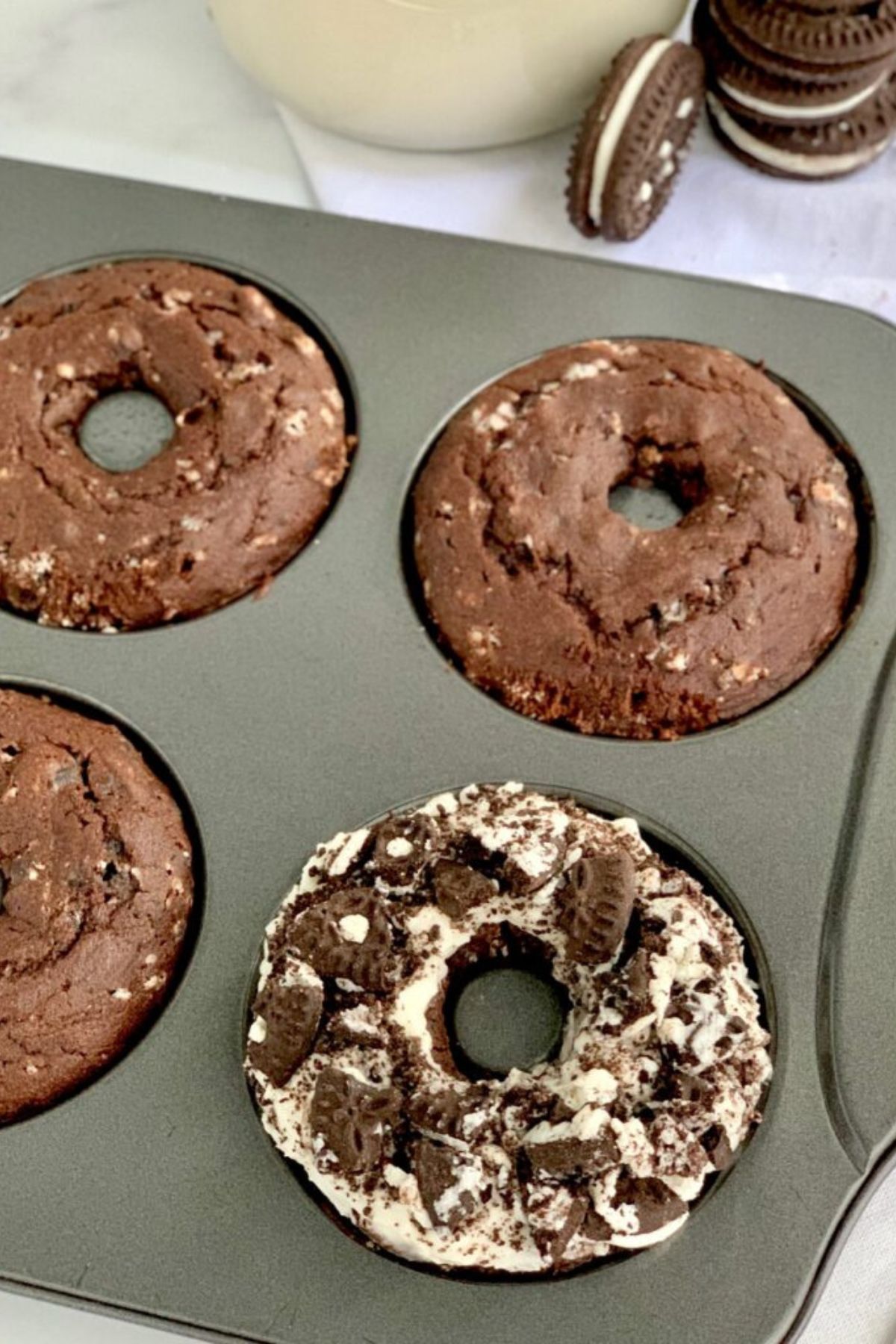 Oreo donuts in a donut pan and one of the donuts is iced and sprinkled with crushed oreo cookies.