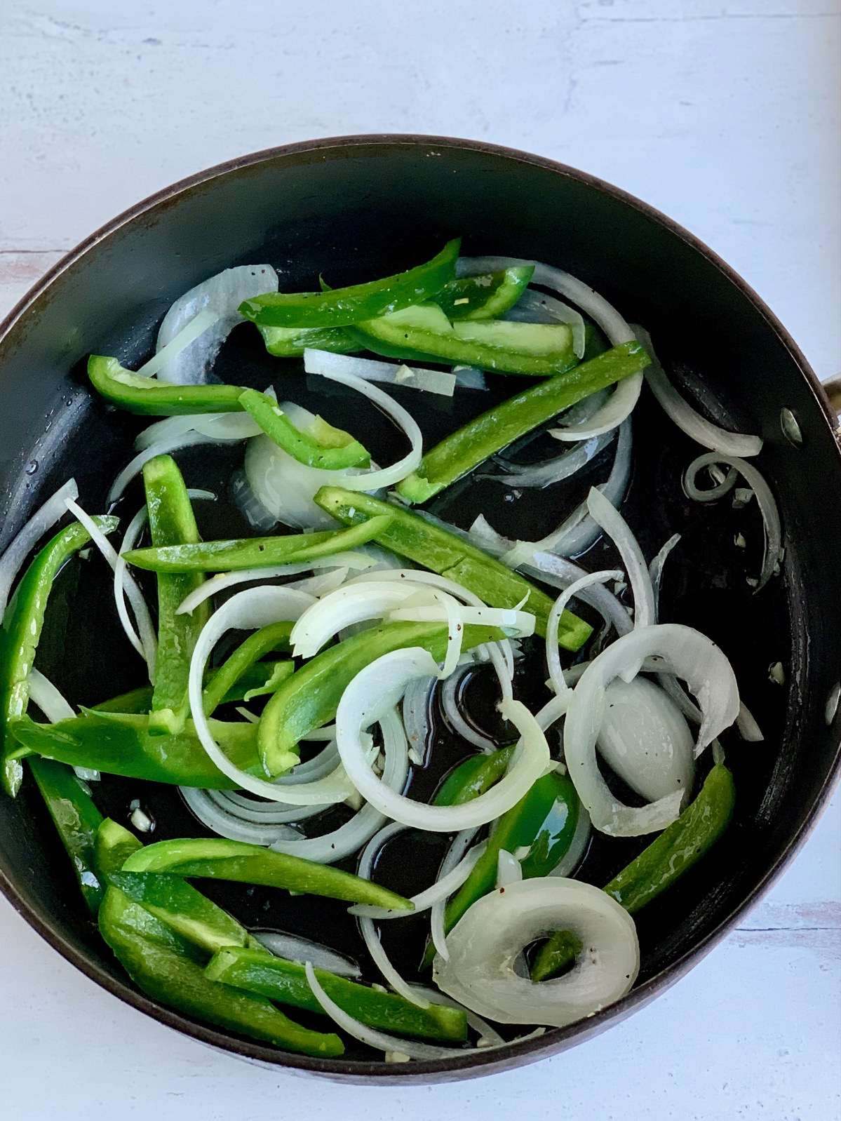 Sautéing sliced onions, garlic, and green bell peppers in a skillet