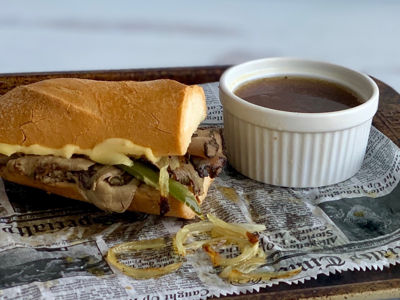 Tender roast beef slices with sautÃ©ed onions and bell peppers with melted cheese layered between a sliced baguette next to a ramakin full of au jus.