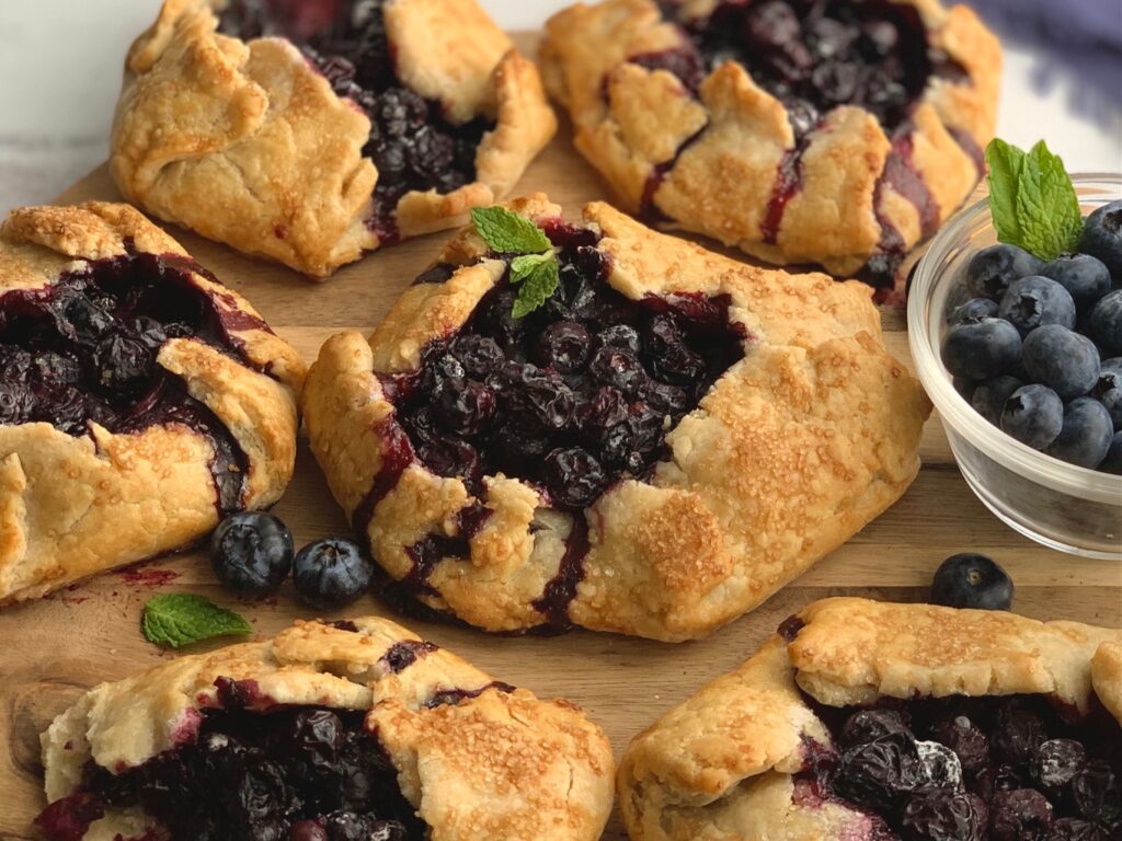 A flat pie dough with sides to keep a blueberry filling inside. With a garnish of fresh mint on top.