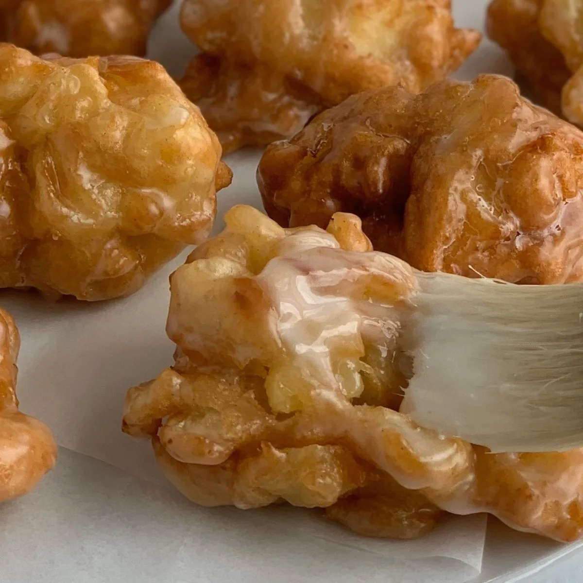 Close up looking at a gluten-free apple fritter and a pastry brush brushing a homemade glaze on it.