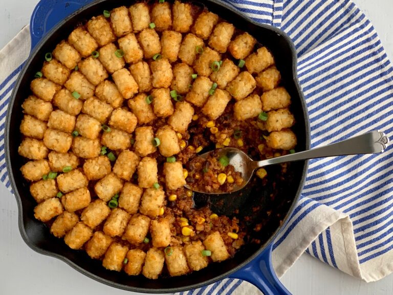 Tater tots on top of a taco mixture of ground beef, corn, black beans, and sauces.
