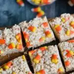 Rice krispie cereal with melted marshmallow over it and candy corns on top cut into large squares.