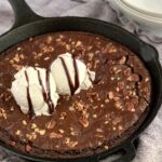 Baked brownie in a cast iron pan with walnuts, ice cream, and chocolate syrup on top