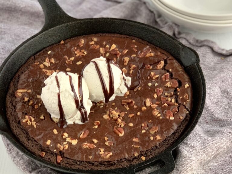 Baked brownie in a cast iron pan with walnuts, ice cream, and chocolate syrup on top