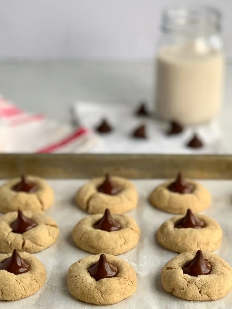 A baking sheet full of peanut butter sugar cookies after they've come out of the oven with chocolate kisses on them