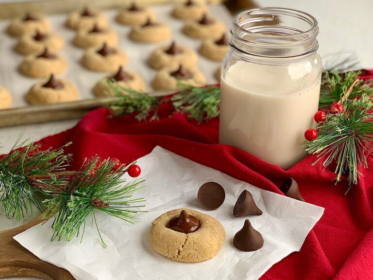 Peanut butter cookies with a softened homemade chocolate kiss in the middle next to a glass of dairy free milk