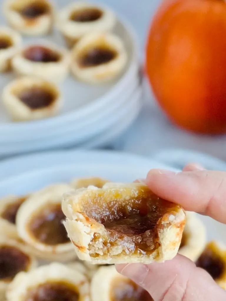 A hand holding a mini little baked tars filled with a brown sugar gooey mixture.