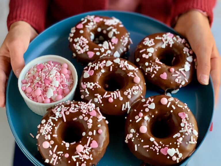 A blue plate with chocolate donuts on it. They have small white and pink sprinkles on them.