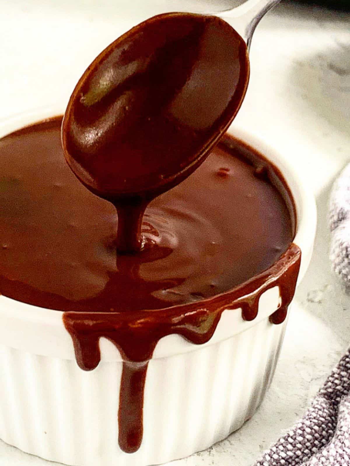 Rich chocolate ganache in a white ramekin with a spoonful being poured.