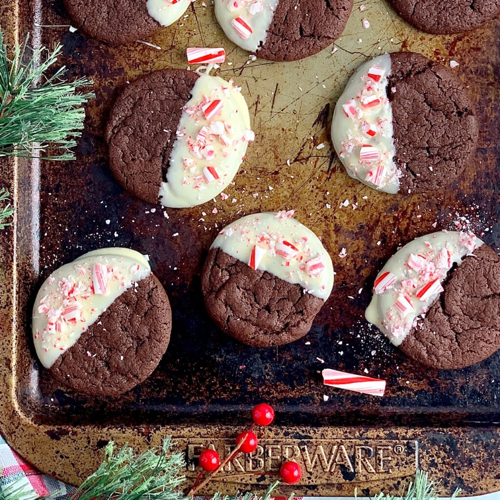 chocolate peppermint cookies dipped in melted white morsels with crushed candy canes on a cookie sheet