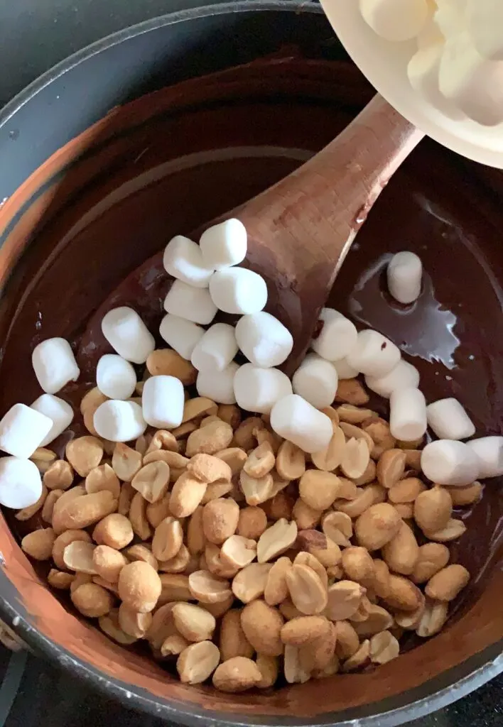 salted peanuts and marshmallows in a saucepan of melted chocolate