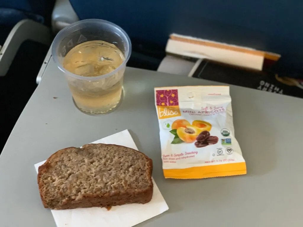 A slice of banana bread, and other snacks on an airplane tray table