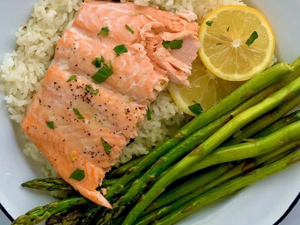 Flaky salmon on a bed of white rice with a side of asparagus.