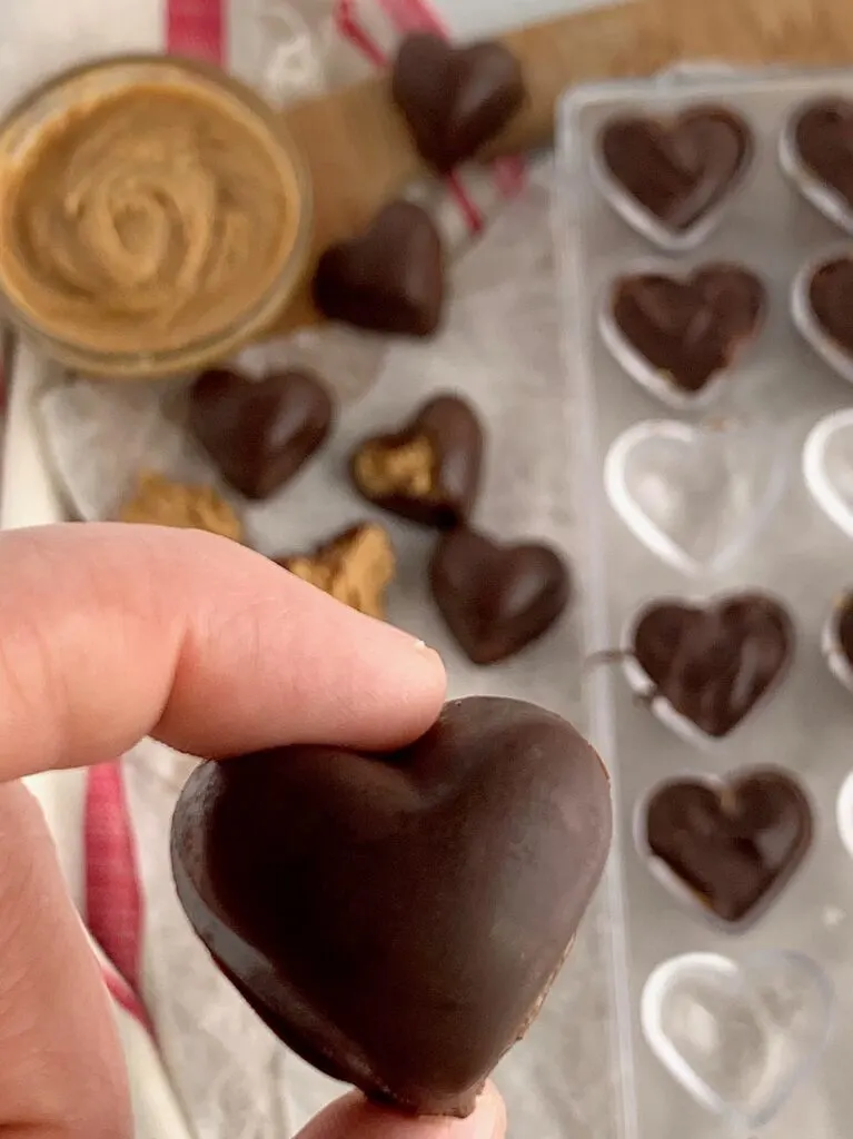 a hand holding a chocolate covered peanut butter heart