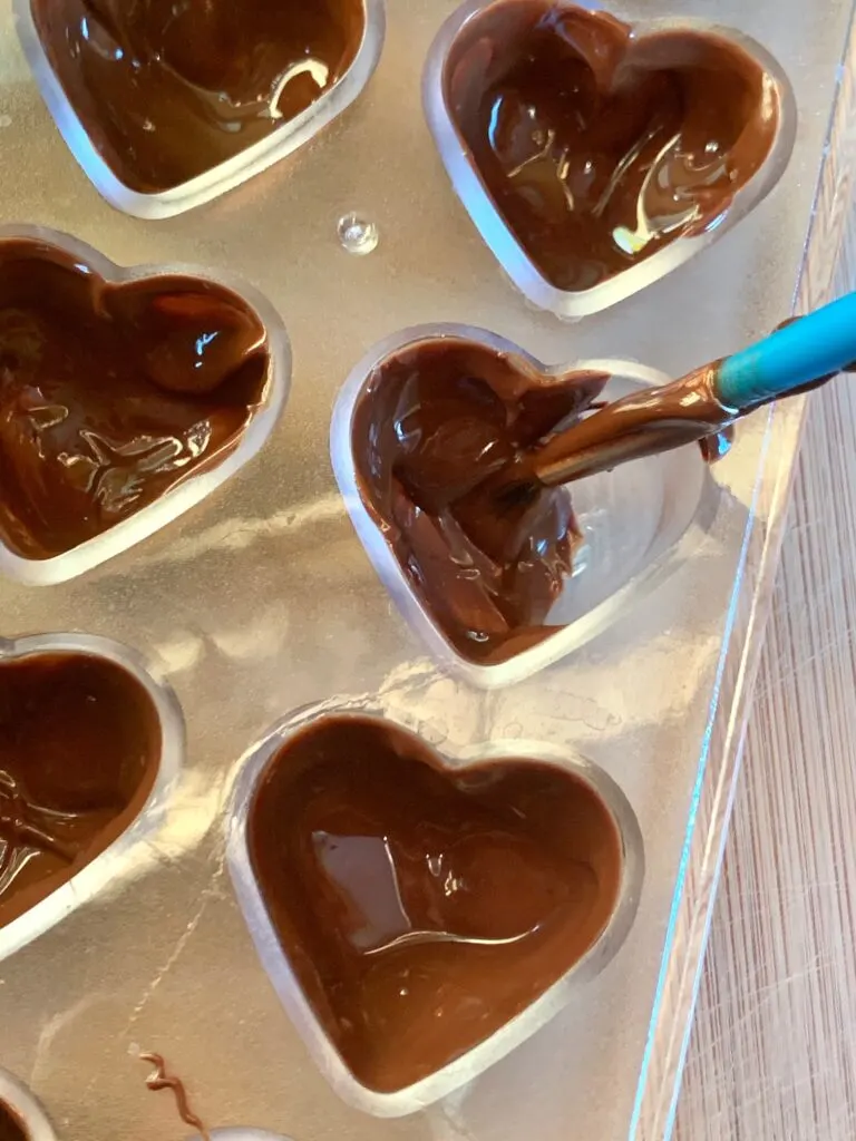 a paint brush painting melted chocolate inside of a plastic heart mold