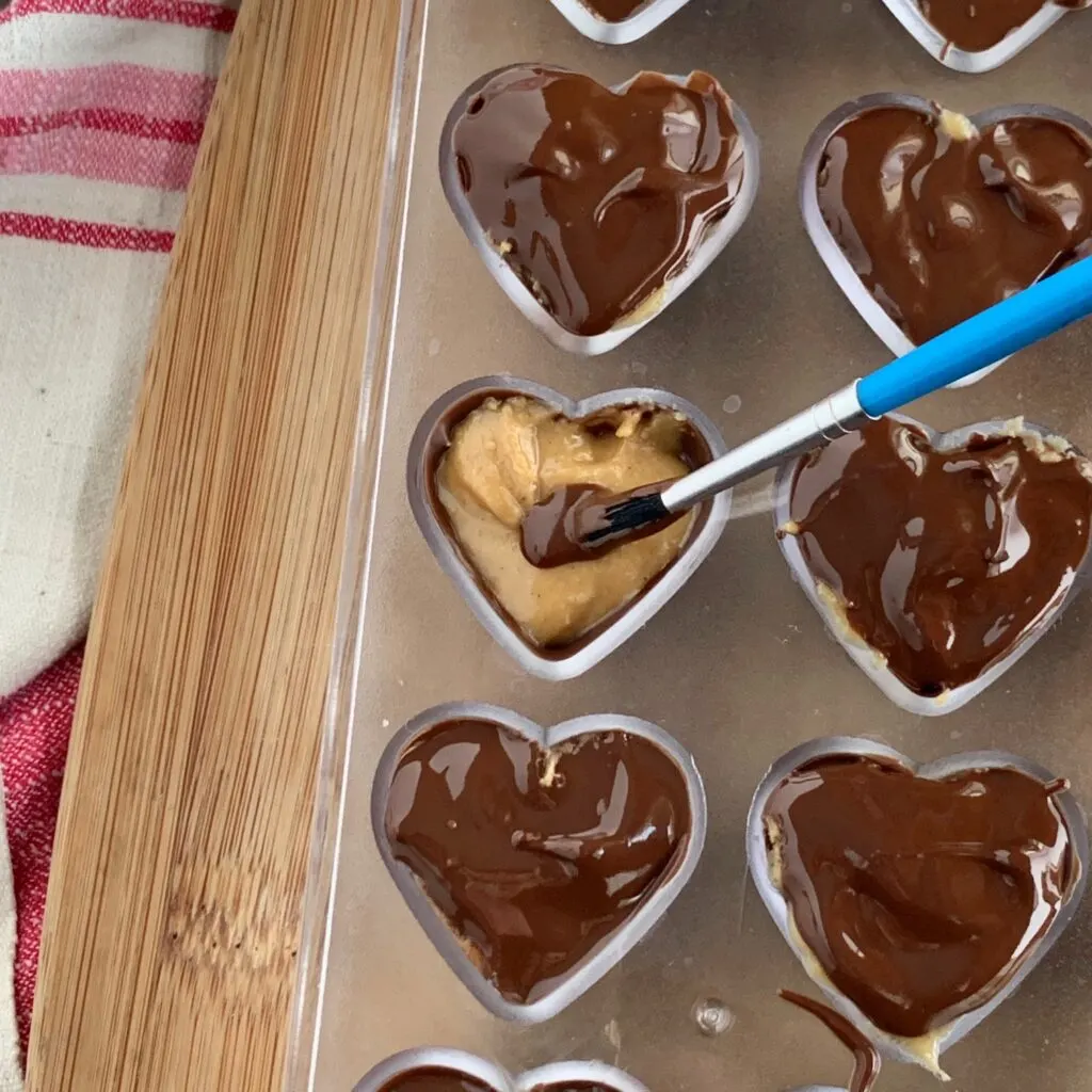 a paint brush painting melted chocolate over peanut butter heart