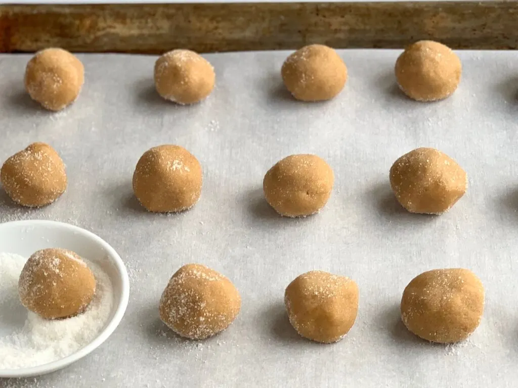 Peanut butter blossom dough rolled into balls with sugar