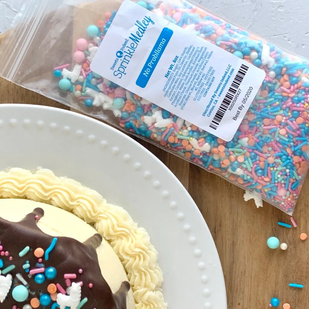 gluten and dairy free cake with chocolate ganache dripping down the edge and sprinkles in a bag