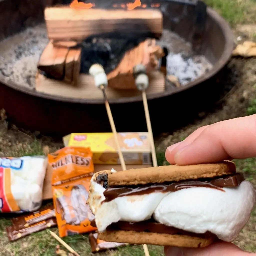 A s'more with melted chocolate oozing out by the campfire