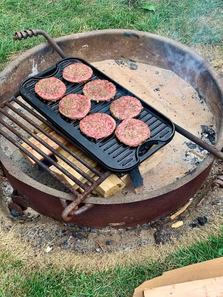 Hamburgers grilling over an open fame on a large cast iron griddle
