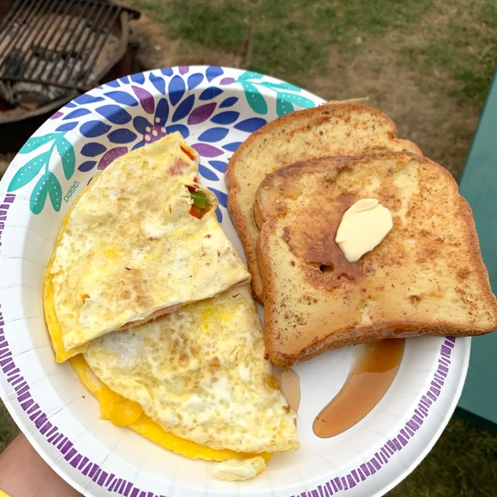 A plate with an omelet and two slices of french toast and syrup