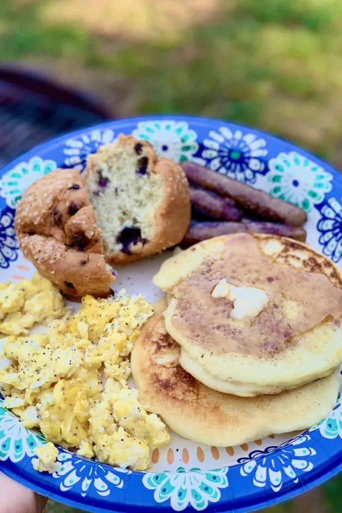 A plate full of allergen safe foods such as scrambled eggs, blueberry muffins, sausage links, and two pancakes smothered in maple syrup. 