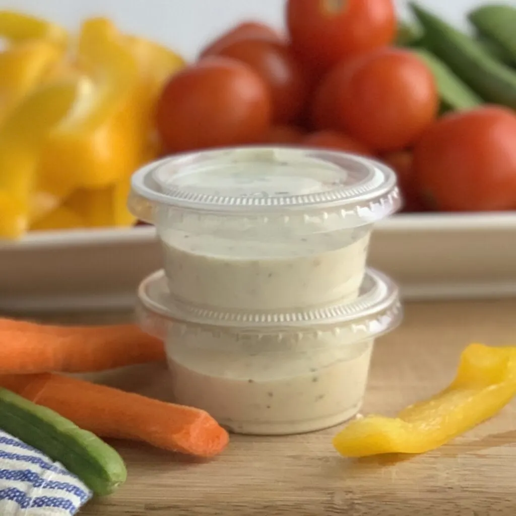 Two small plastic containers of dairy free ranch dressing.