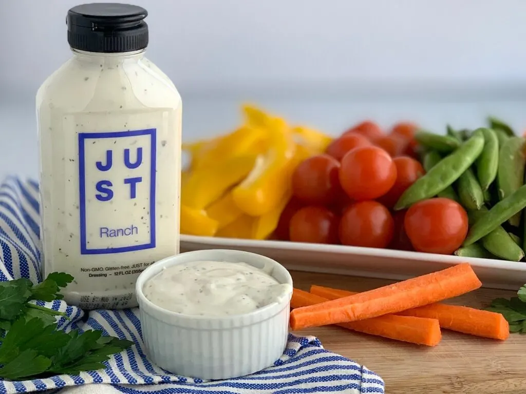 A container of Just Ranch dressing next to a platter of fresh vegetables. 