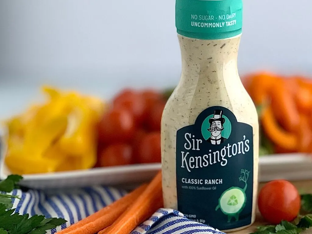 A bottle of Sir Kensington's Classic Ranch dressing next two carrots and a vegetable platter.