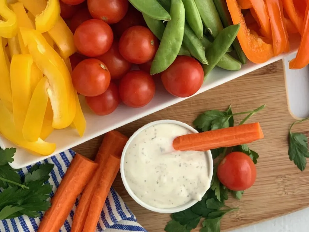 A plate covered in fresh vegetables with a small bowl of dairy free ranch dressing on the side.