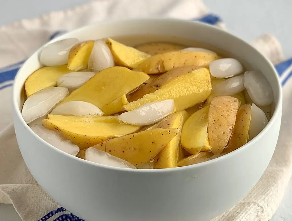 Potato wedges in a large bowl filled with ice water.