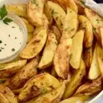 A plate heaping of baked potato wedges with dressing.