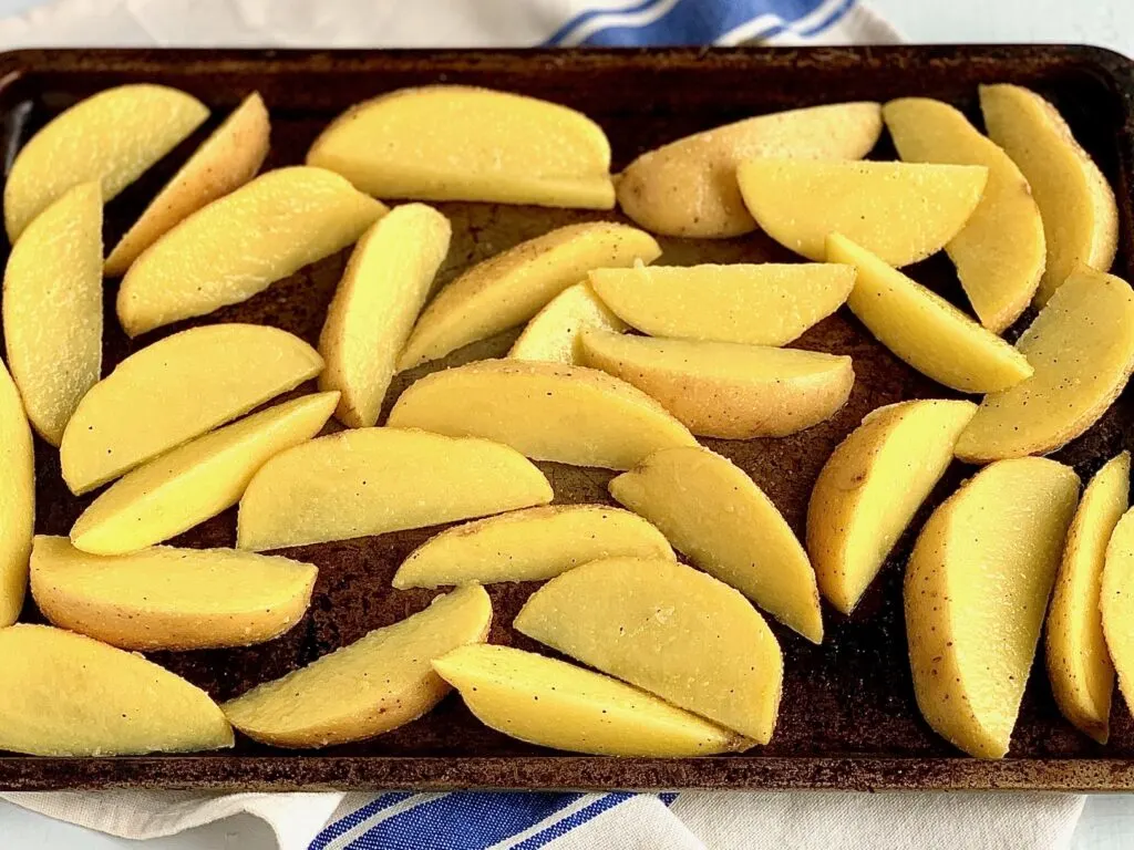 Seasoned potato wedges on a baking sheet ready for the oven