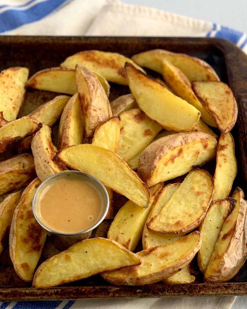 baked potato wedges on a baking sheet with a small container of Copycat Chick-Fil-A Sauce