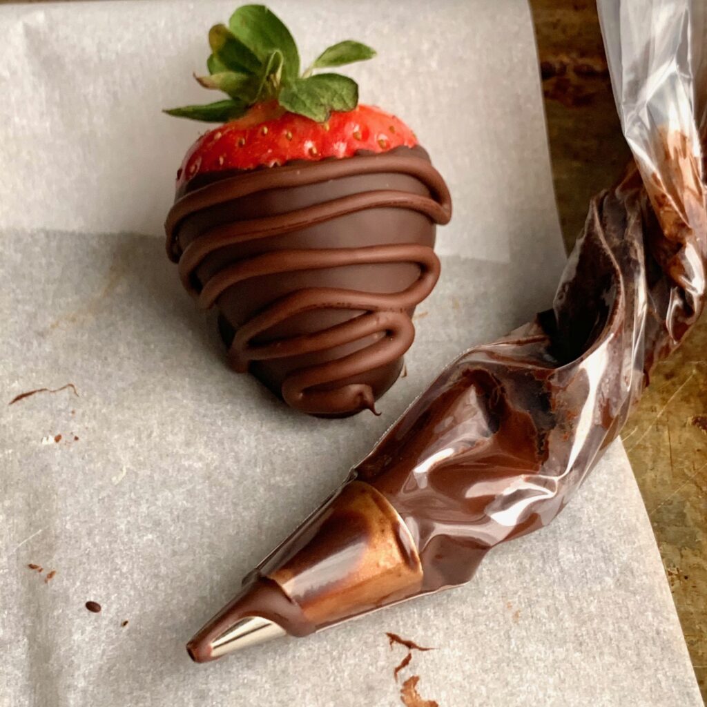 a chocolate covered strawberry with melted chocolate in a piping icing bag