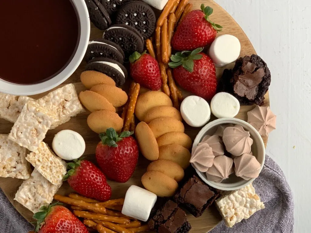 A dessert platter with strawberries, mini brownie bites, pretzel rods, oreo sandwich cookies, marshmallows, mini rice krispie treats and ganache dipping sauce.