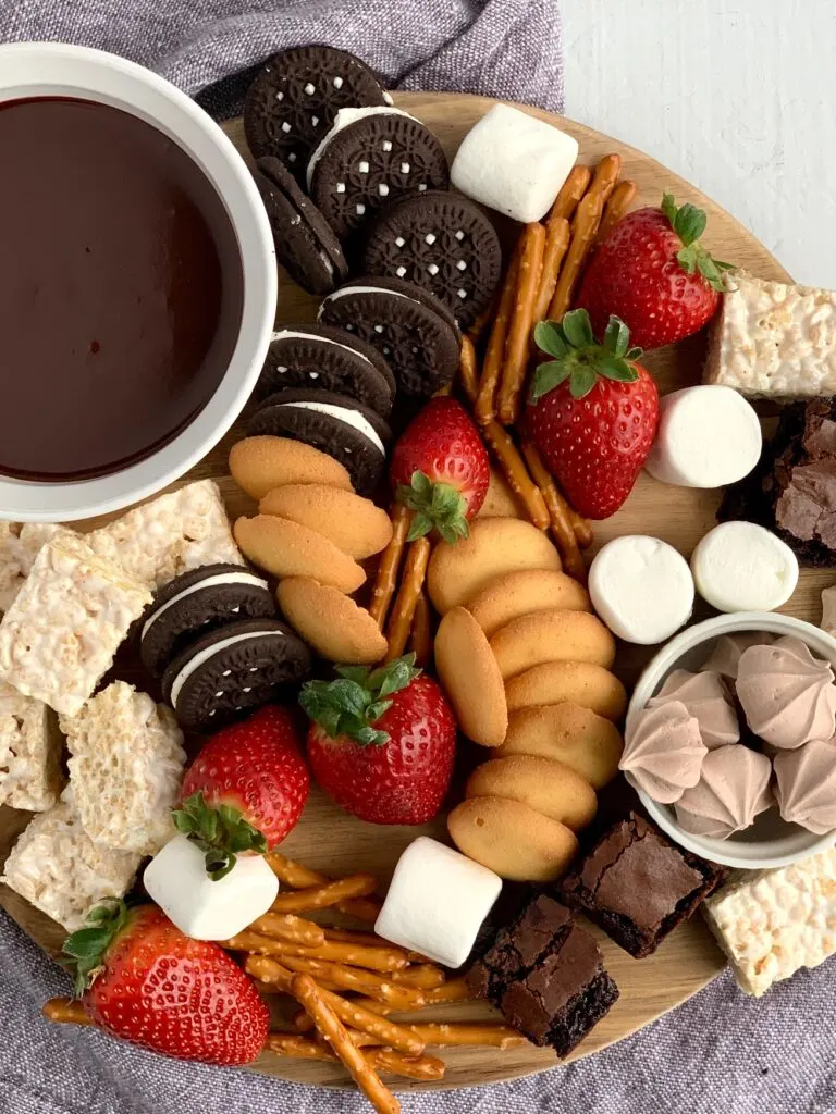 A dessert platter with strawberries, mini brownie bites, pretzel rods, oreo sandwich cookies, marshmallows, mini rice krispie treats and ganache dipping sauce.