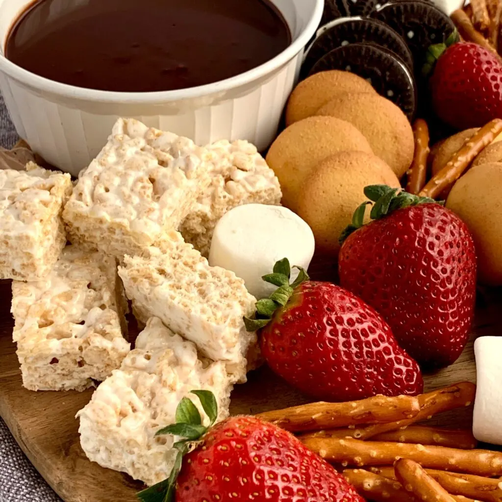 A dessert platter with strawberries, mini brownie bites, pretzel rods, oreo sandwich cookies, marshmallows, mini rice krispie treats and ganache dipping sauce.