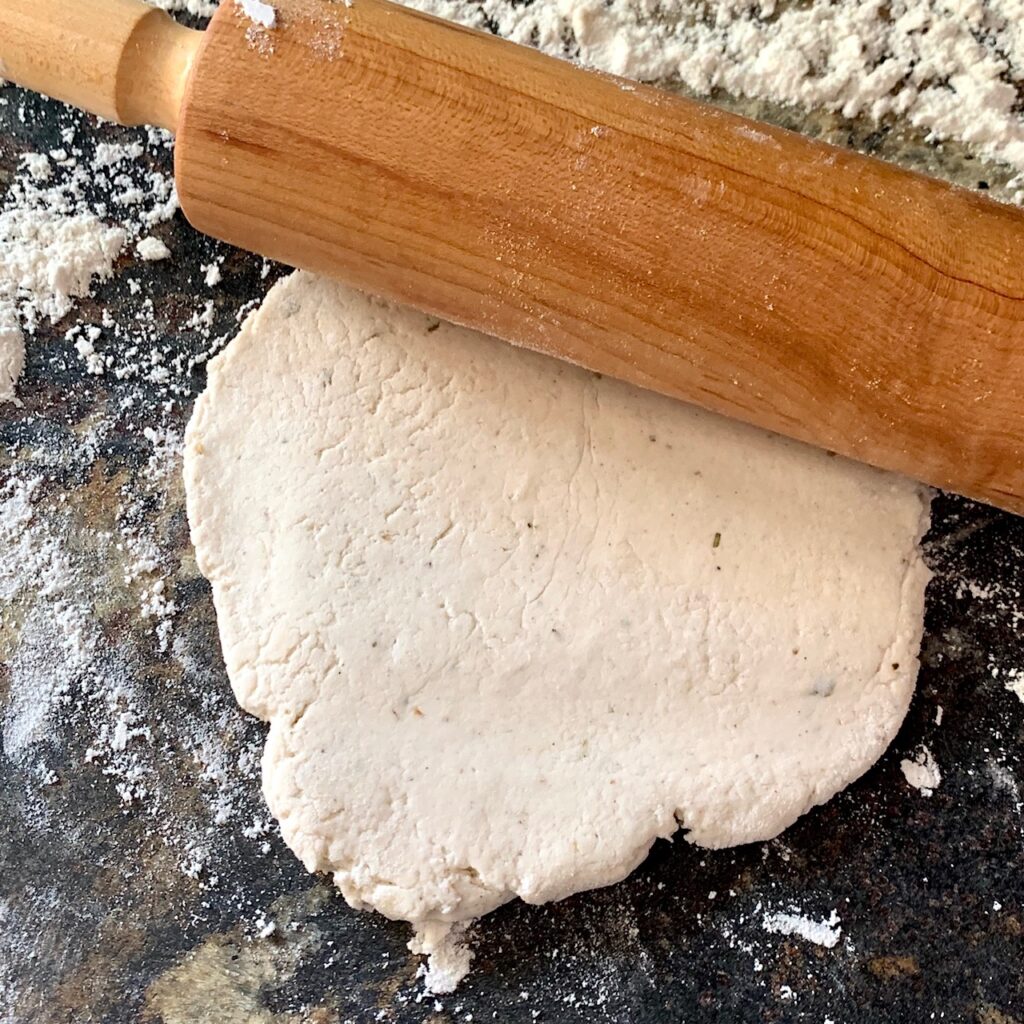 flat round of pizza dough with a rolling pin