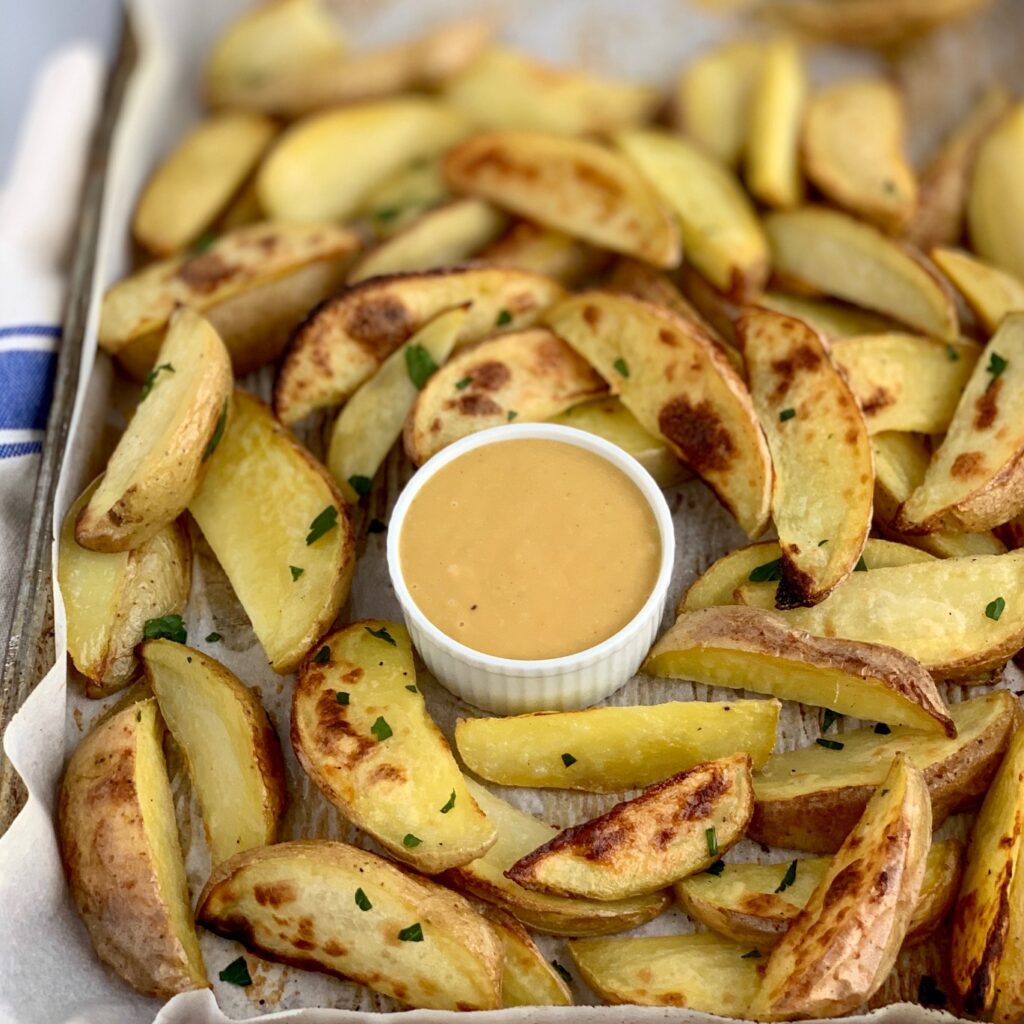 A large sheet pan of baked potato wedges surrounding a bowl of homemade Chick-Fil-A Sauce
