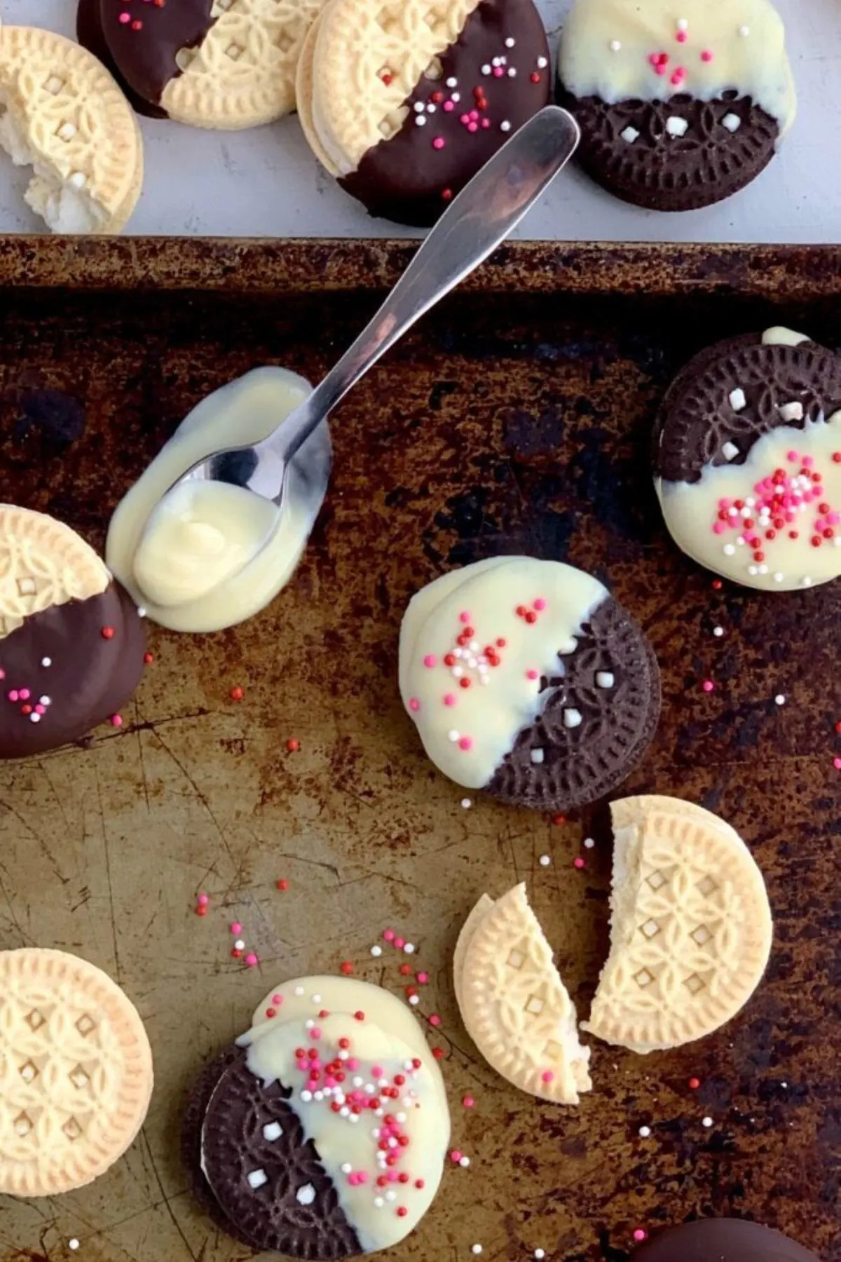 A spoon with melted dairy free chocolate on a baking sheet with more coated cookies.