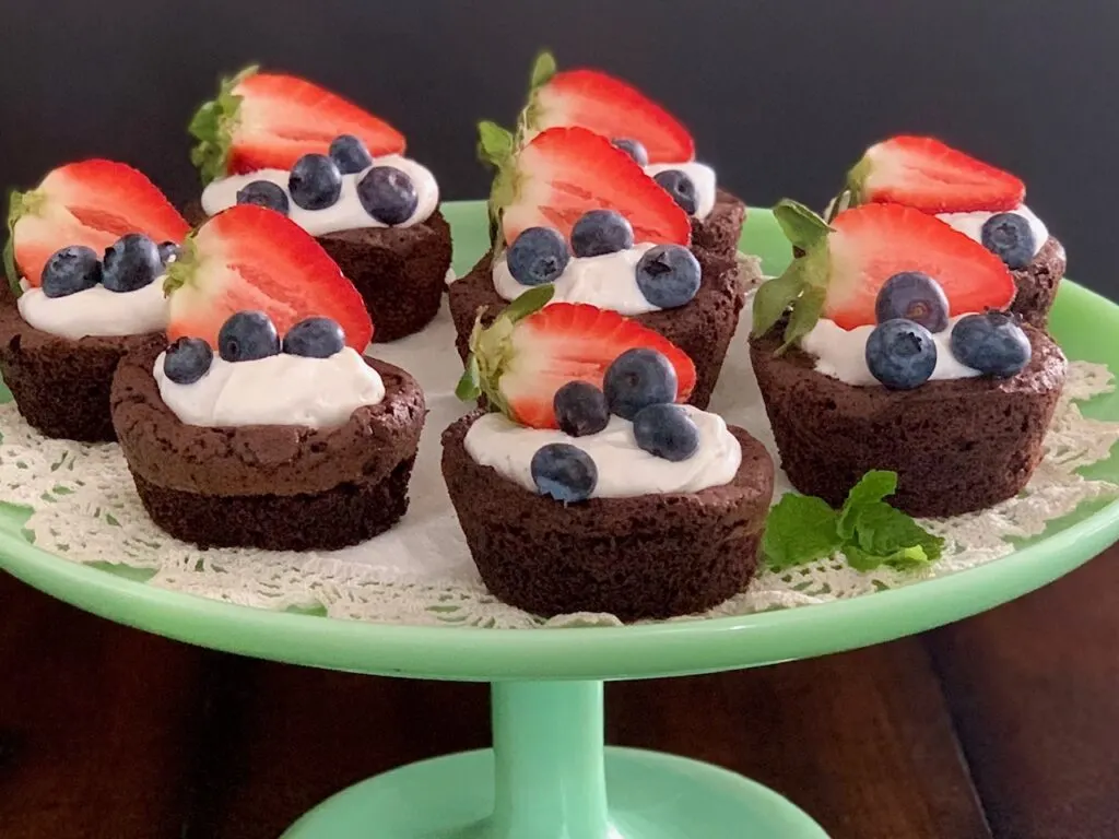 A plate of homemade brownie bites with whipped topping and fruit.