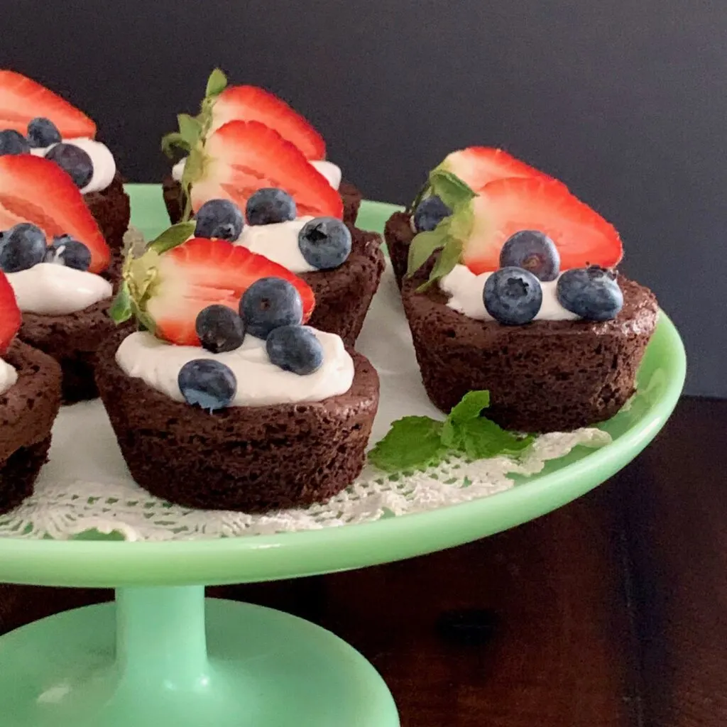 Homemade brownie bites on a serving tray topped with dairy free whipped topping and fruit. 